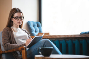 Portrait of mindful attractive young female sitting in modern cafe interior near huge window and copy space