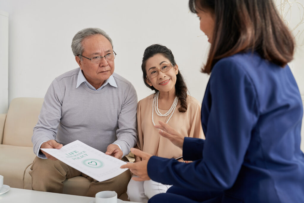 Back view of friendly agent in formalwear explaining details of life insurance program to senior clients while having meeting at cozy office