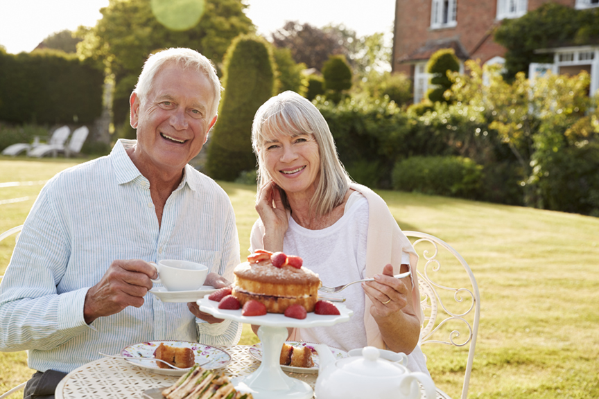 Retired Couple Enjoying Afternoon Tea In Garden At Home