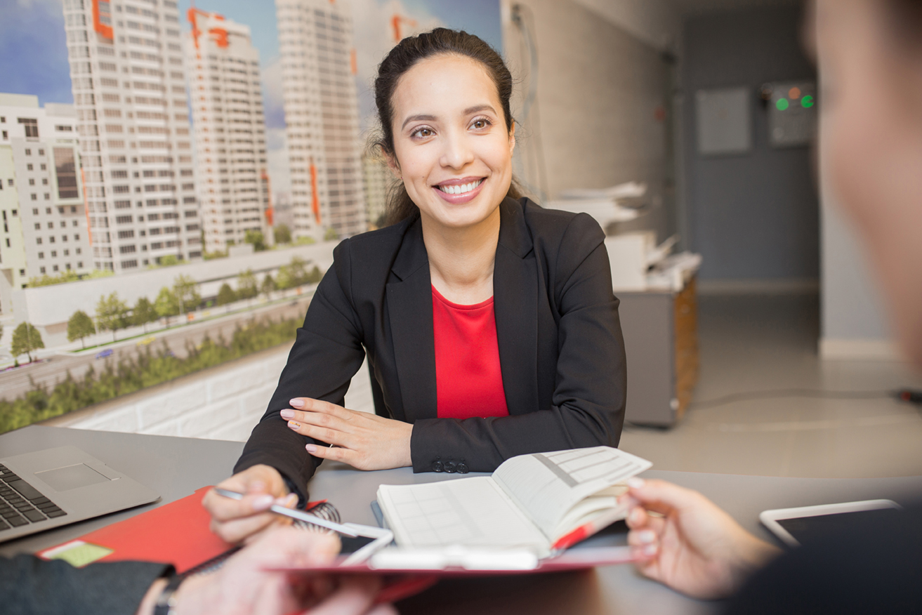 Portrait of friendly mixed-race woman smiling happily while talking to client in real estate agency