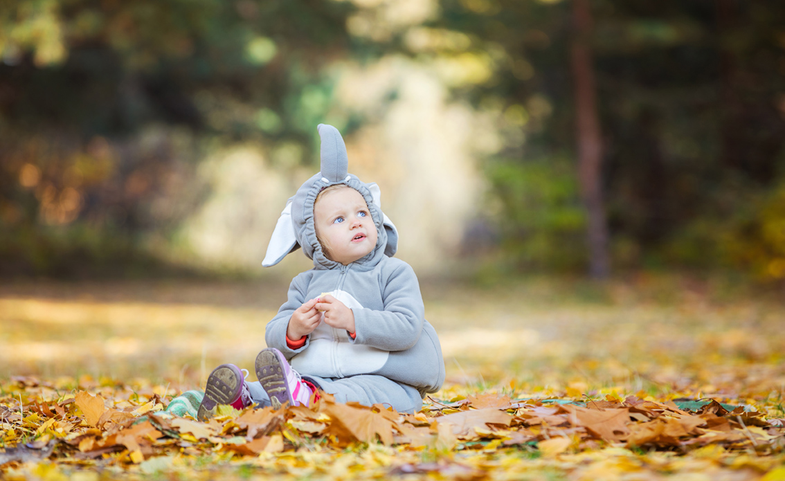 Cute little girl in elephant costume looking up while playing in autumn forest