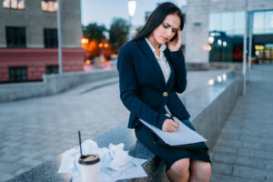 Tired businesswoman works outdoor, financial statements, business center on background. Modern building, cityscape. Female businessperson